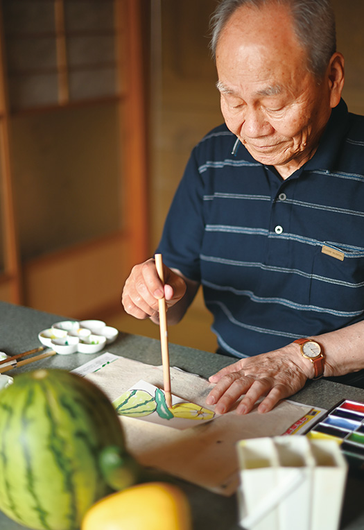 自宅の一室で制作に没頭する河合さん。おすそ分けのスイカやキュウリを前に